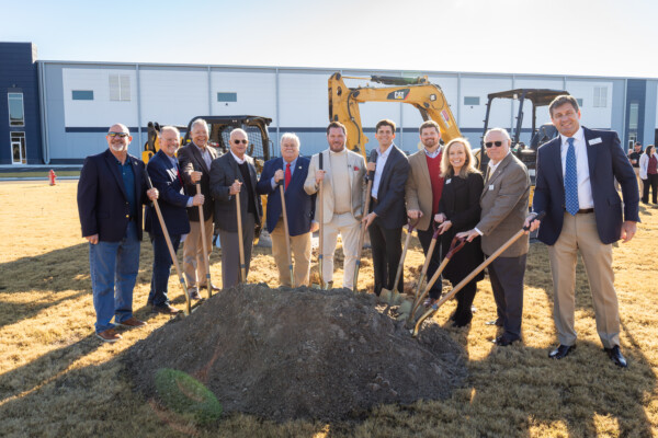 A group of people in business attire pose with shovels at a groundbreaking ceremony in front of construction equipment and a modern building, celebrating Downtown Brunswick 2026 Downtown of the Year.