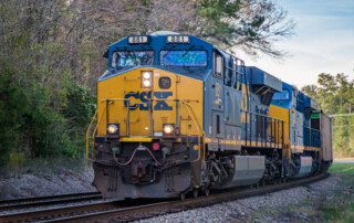 A CSX freight train with locomotive number 881 travels on railroad tracks through a wooded area near the CSX Select Site Georgia Breakbulk Logistics Park during the day.