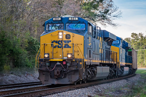 A CSX freight train with locomotive number 881 travels on railroad tracks through a wooded area near the CSX Select Site Georgia Breakbulk Logistics Park during the day.